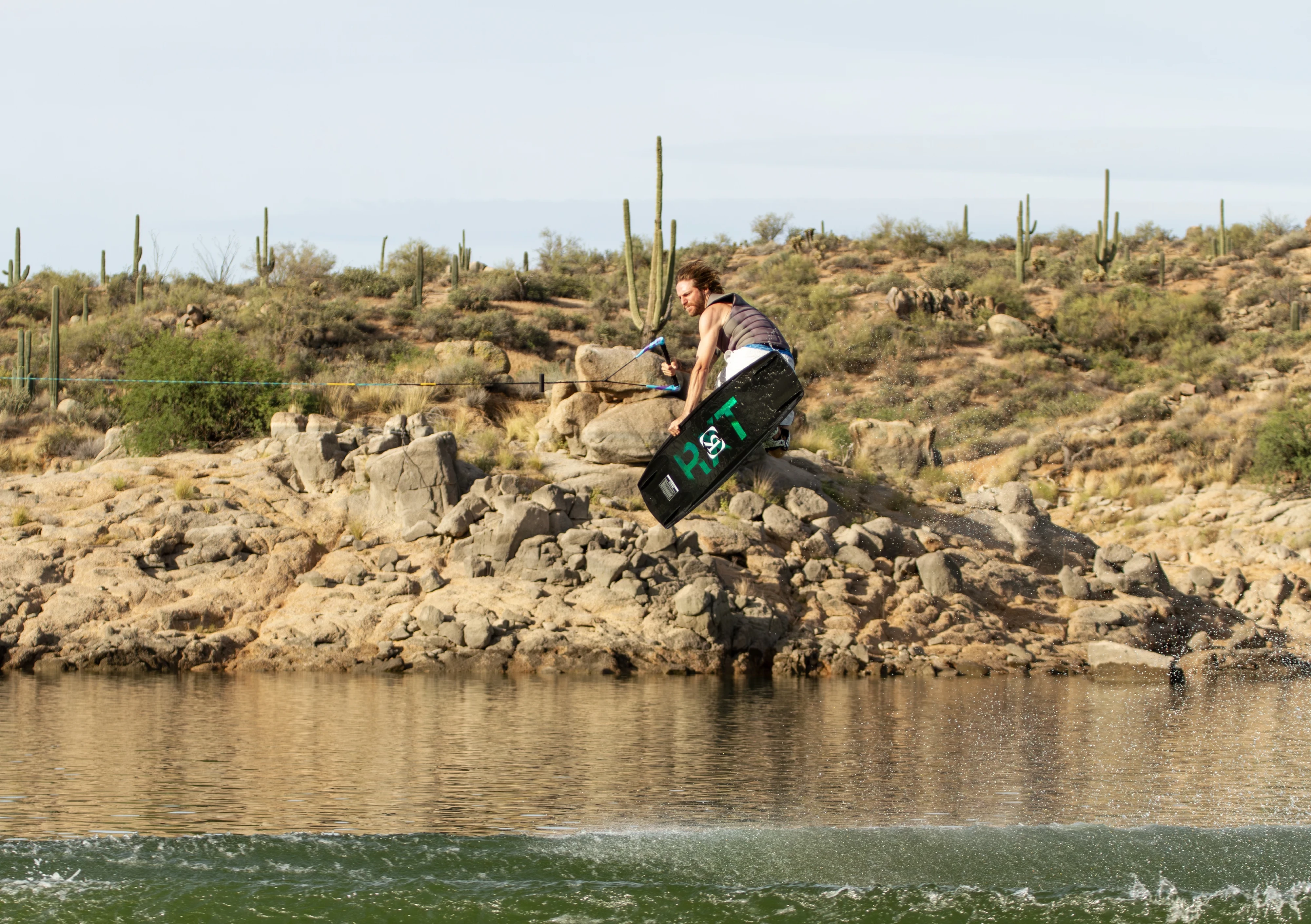 Action shot of Massi Piffaretti riding the Ronix RXT - Ronix Xperiemental Technology, with water, rocks, cacti in the background